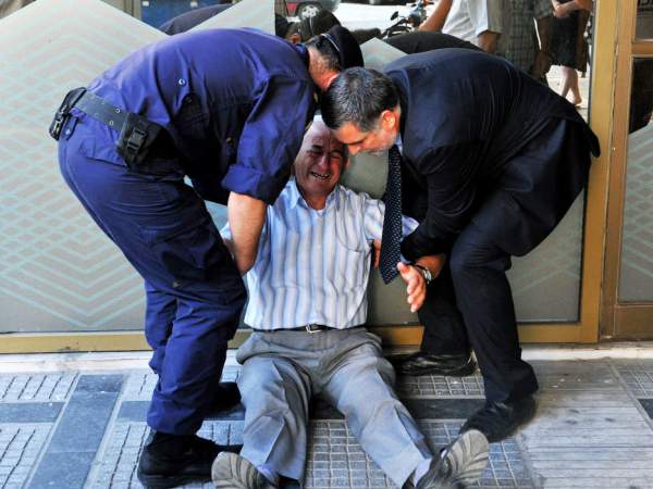 Aposentado grego chora na fila em agência bancária em Atenas nesta sexta-feira (3) (Foto: Sakis Mitrolidis/AFP)